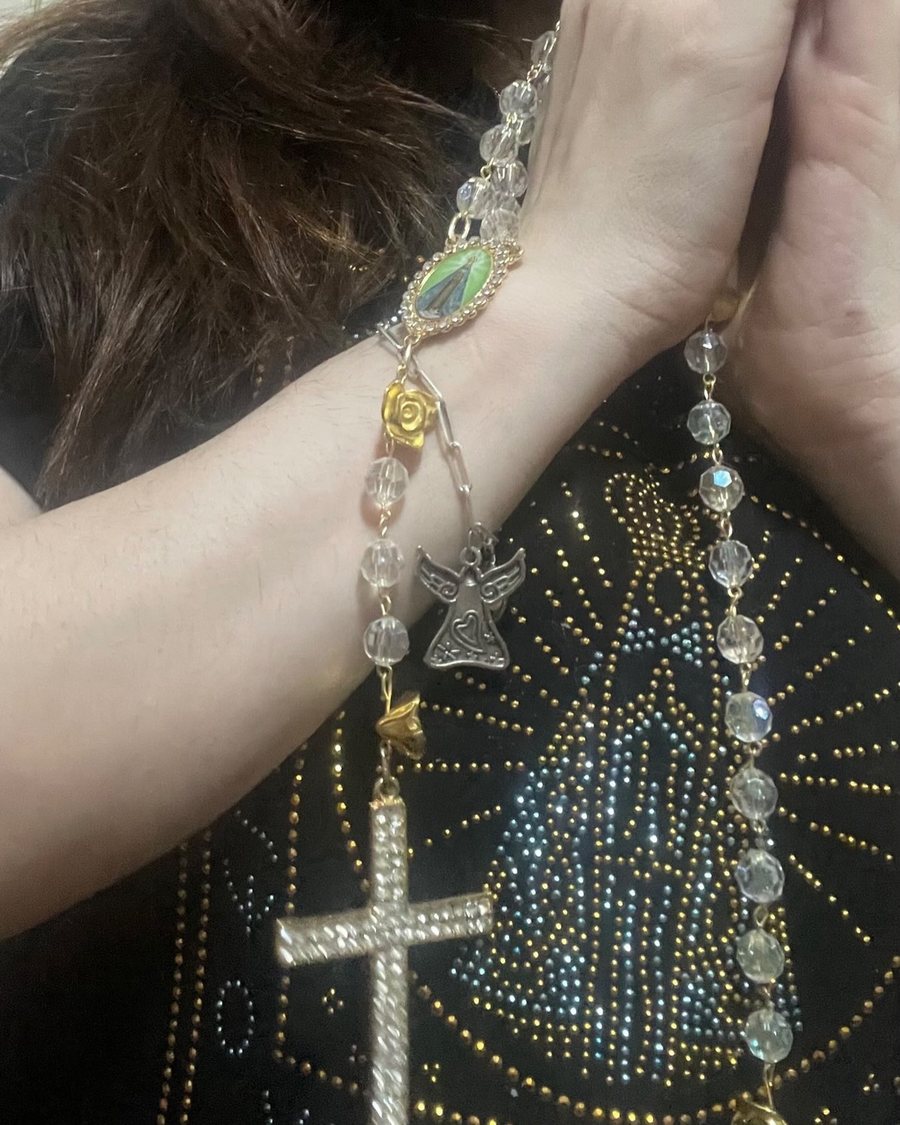 Mãos em oração segurando um terço de cristal do ateliê